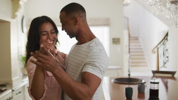 Happy biracial couple dancing together in kitchen