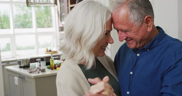 Romantic senior caucasian couple at home dancing in the kitchen and smiling