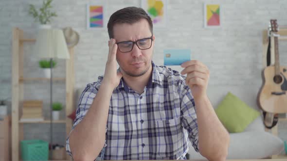 Sad Young Man with Credit Card in Hand Sitting at a Table in a Modern Apartmentconcept the Idea of