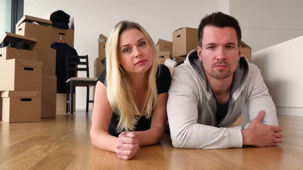 A Moving Couple Lies on the Floor of an Empty Apartment and Looks Seriously at the Camera