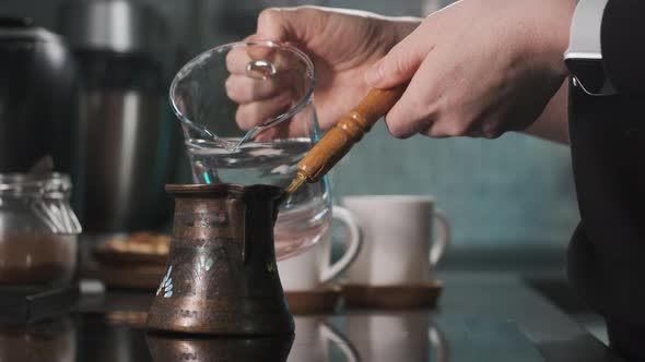 Woman Prepares Coffee in Turk on the Burner in the Kitchen