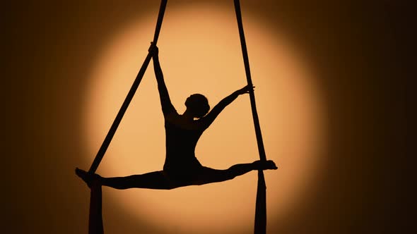 Silhouette of a Young Woman Performs Acrobatic Elements and Twine on Airy Silk