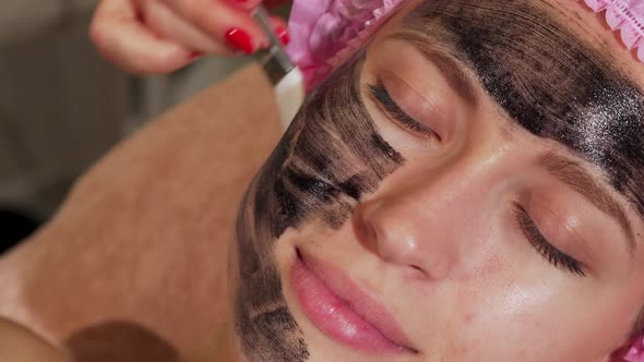 Woman Having Black Facial Mask Being Applied on Her Face By Cosmetologist