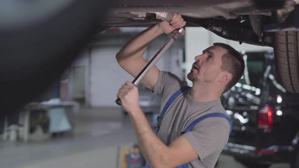 Portrait of Professional Caucasian Auto Mechanic Tightening Screws on Car. Young Handsome Man