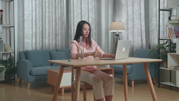 Asian Woman Drinking Vodka While Typing On A Laptop At Home