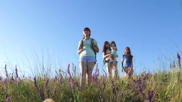 Happy Mom and Daughters, a Little Baby Travel Across the Field with Backpacks in Colors