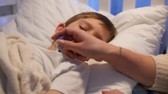 Mother Looking at Thermometer and Checking Body Temperature of Her Sick Little Boy