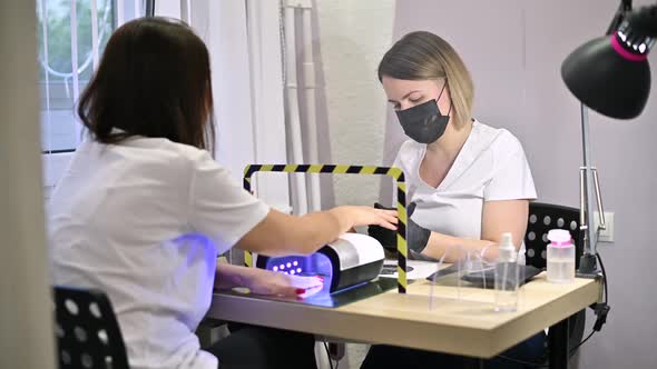 The master in a protective mask and gloves serves the girl in a beauty salon