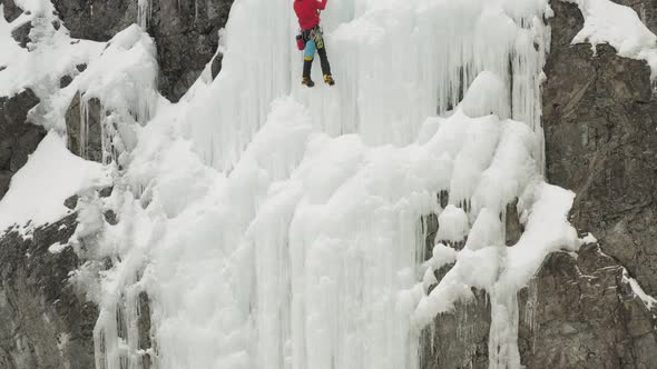 Climber climbs frozen ice sheet cascade with axes aerial 4K