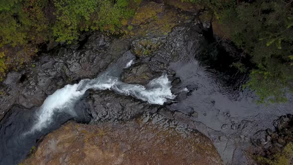 aerial top down overhead shot of river flowing in the forest creating white raging rapids.