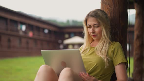 Attractive Lady Reads News in Social Media Laptop on Terrace