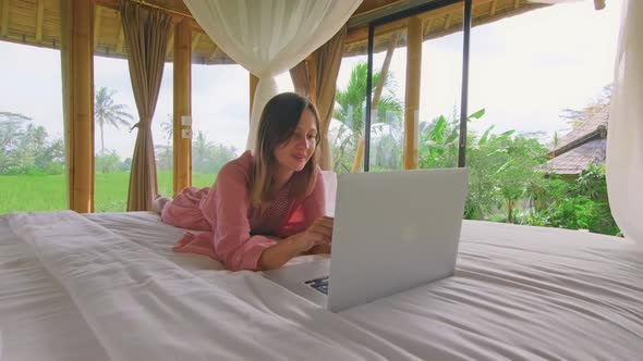 Young Woman Chatting Via Internet in Eco Bamboo House Standing in Rice Fields