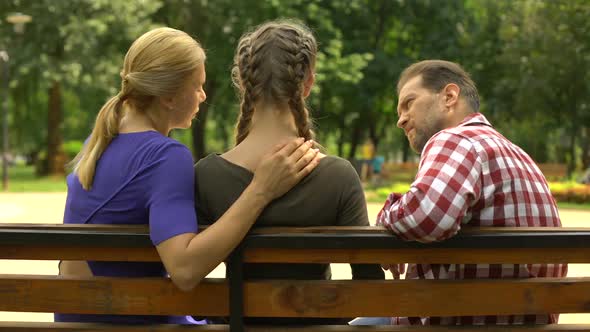 Loving Parents Supporting Depressed Daughter Sitting on Bench in Park, Sadness