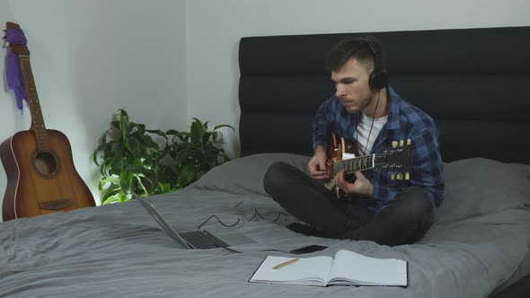 Guitar player learning new chords on electric guitar on bed at modern home. Music concept