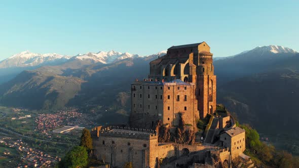 Aerial: drone flying at old medieval abbey perched on mountain top at sunrise, Turin italian Alps