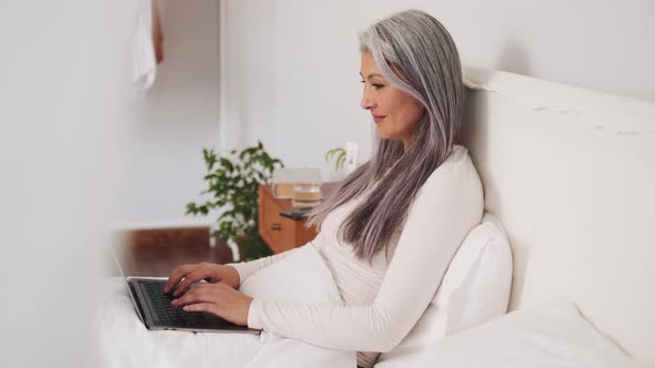 Side view of Asian woman typing by laptop