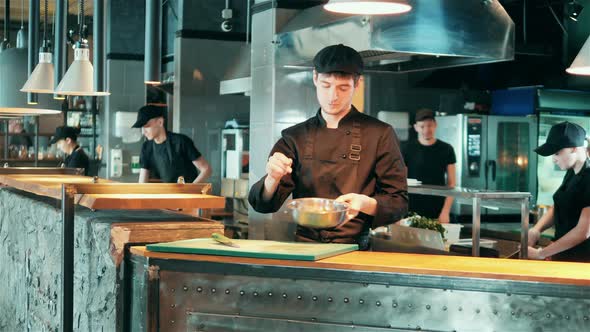 Male Chef is Seasoning and Tossing Food in a Bowl