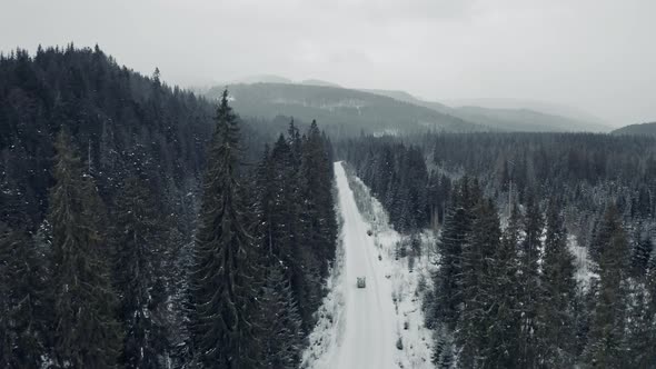 Aerial View From Drone on Car Driving Through Winter Snow Covered Forest