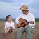 Little Boy and His Father Playing Guitar at Hay Bale in Field - VideoHive Item for Sale