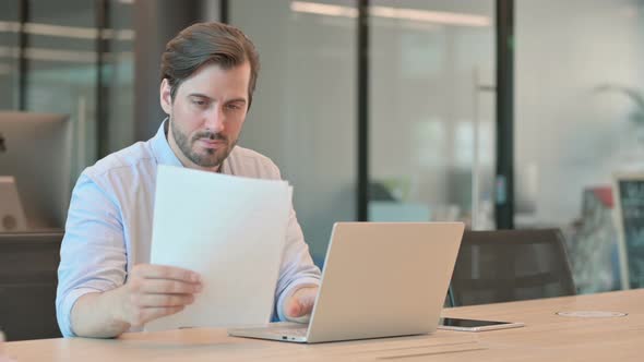 Man with Laptop Reading Documents