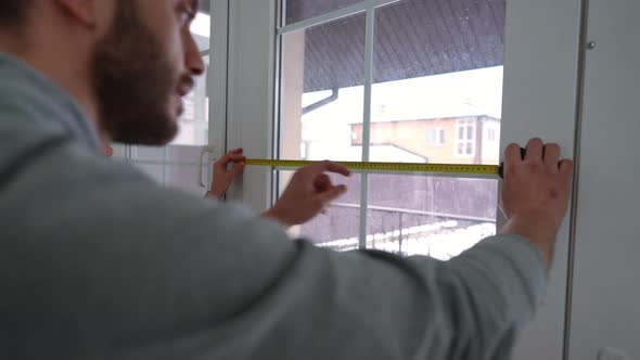 Concentrated Man Measuring Window with Ruler Indoors Talking with Woman