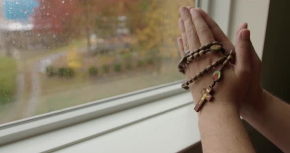Close Up Tilt of Hands in Prayer Holding Rosary Beads
