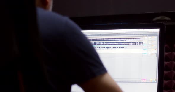 A Music Producer is Sitting at a Computer in a Recording Studio