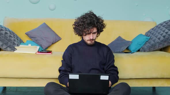 Young Man is Browsing at His Laptop and Stretches Up His Hands Working at the Laptop