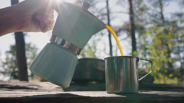 Person Hands Pour Hot Drink to Mug on Table Against Forest