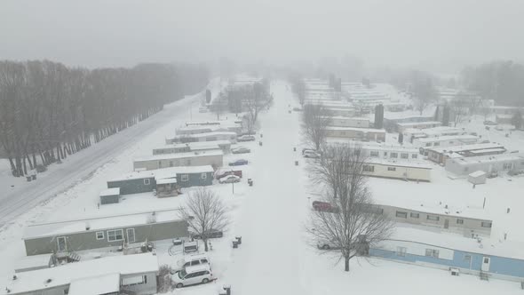 Aerial view over mobile home park in winter with county road and line of trees.