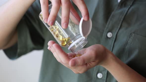 woman pours white pills from a transparent jar into her hand