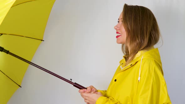 A girl in a yellow raincoat under an umbrella stretches out her hand to the rain.