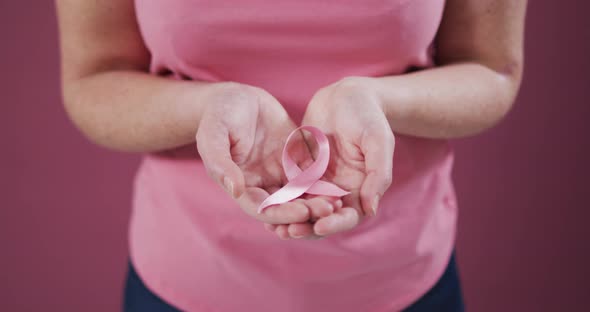 Midsection of woman with hands cupped holding pink breast cancer awareness ribbon