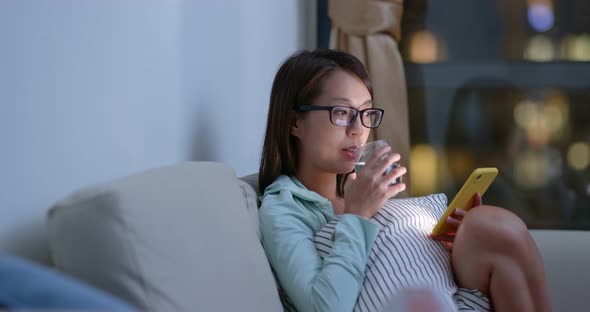 Woman drink of water and use of mobile phone at night inside living room