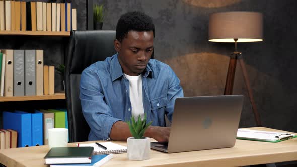 African American Businessman Works for Laptop Turns to Camera and Smiles