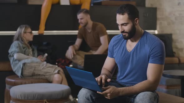 Confident Middle Eastern Man Working Online on Laptop in Casual Coworking As Friends Talking at the