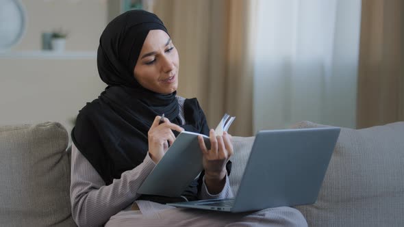 Cheerful Young Muslim Arabian Lady Young Woman Sit on Cozy Sofa Female Freelancer Writer Take Notes