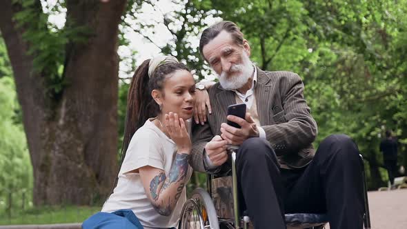 Granddaughter with Dreadlocks and Respected Bearded Retired Granddad in Wheelchair Using Smartphone