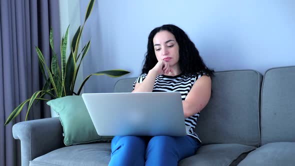 Young Woman Working on Laptop, Sitting on Sofa at Home, Businesswoman Sits at Home Works Remotely on