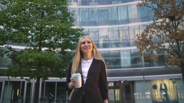 Stylish Business Woman with Coffee on Street. From Below of Serious Blond Executive Girl in Suit