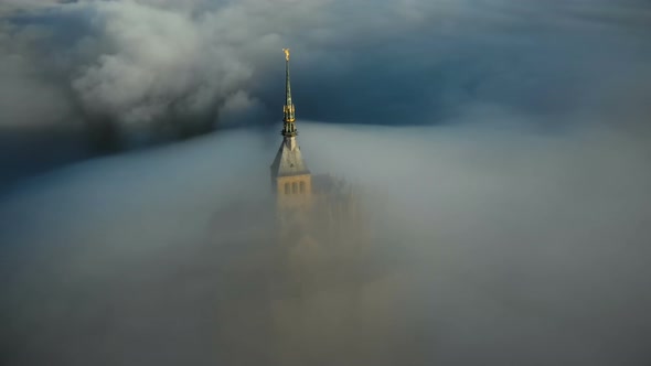 Drone Flying Above Sunrise Mont Saint Michel Castle Steeple Covered By Thick Fog Clouds Flowing Into