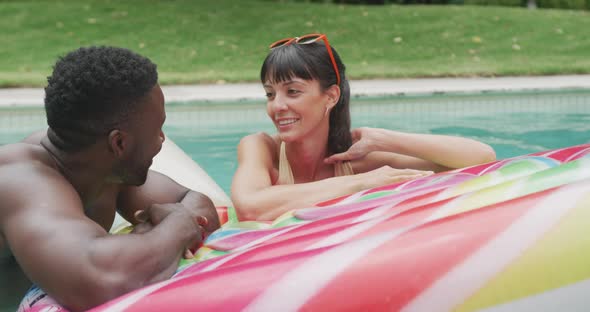 Happy diverse couple wearing swimming suits with inflatable at swimming pool in garden