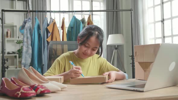 Asian Young Girl Online Seller Writing On Package While Using Computer For Selling Clothes At Home