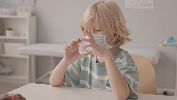 Masked Boy Holding Bottle of Vaccine at Doctor Office