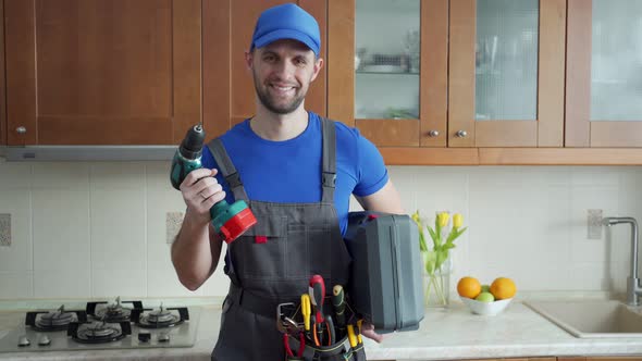 Repairman Holds a Screwdriver and a Suitcase of Tools in the Kitchen and Looks at the Camera