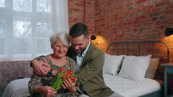 Caucasian Content Grandmother in a Hug with Her Middleaged Businessman Grandson Celebrating