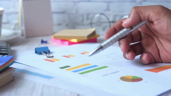 Side View of Man Hand with Pen Analyzing Bar Chart on Paper