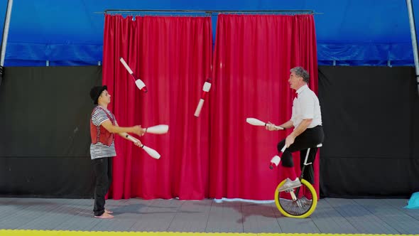 Circus artists juggling clubs sitting on unicycle