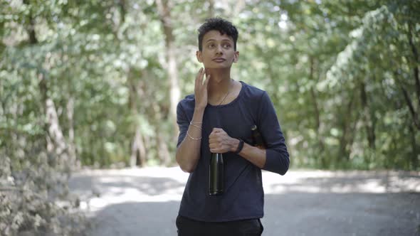 Young Mixed-race Man Walking in Sunlight Outdoors with Beer Bottles. Portrait of Relaxed Addicted