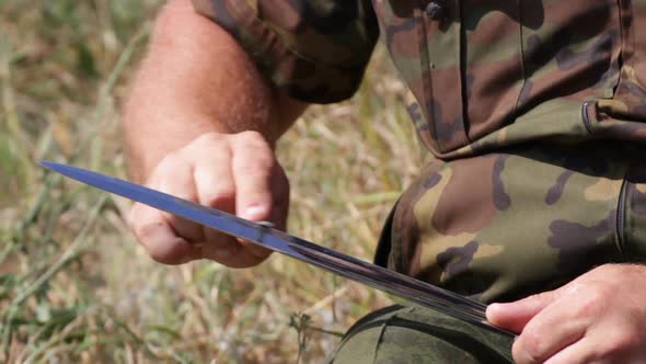 A Man in a Camouflage Uniform Sharpens Cossack Saber